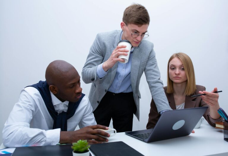 A diverse group of professionals collaborating around a laptop in a modern office setting.