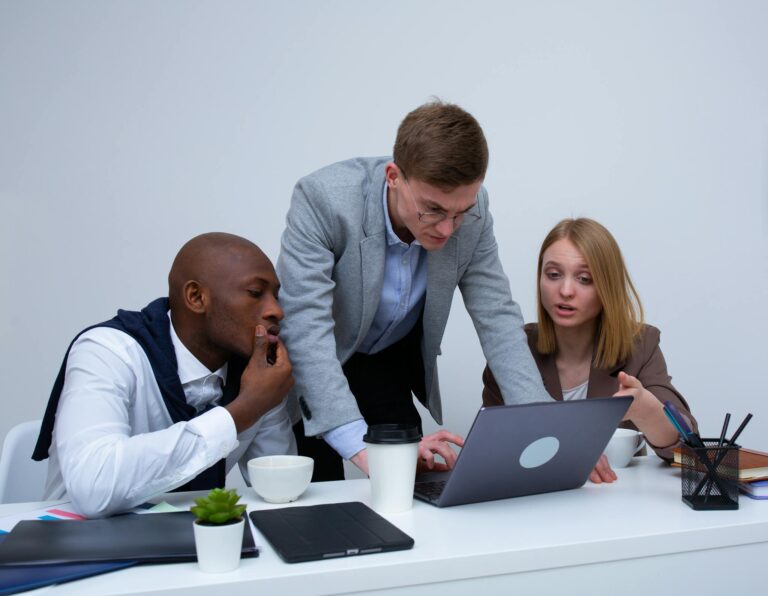 Three colleagues engaged in teamwork around a laptop in a modern office setting.